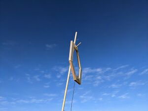 VLF Antenna (Approx 0.8m2, wood, copper wire, audio jack) hanging from a wooden pole against a blue sky.